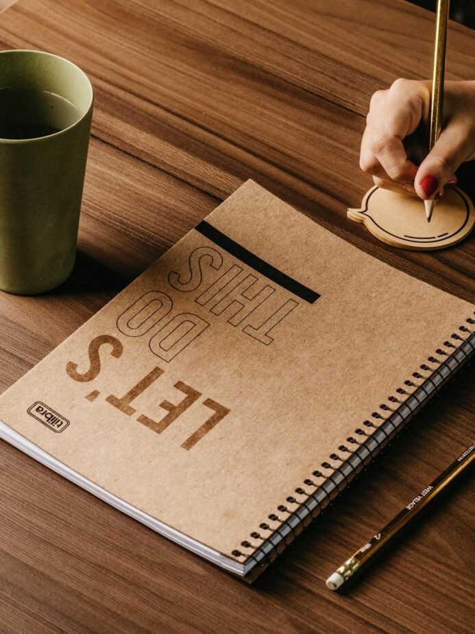 Hands writing notes next to a cup of coffee